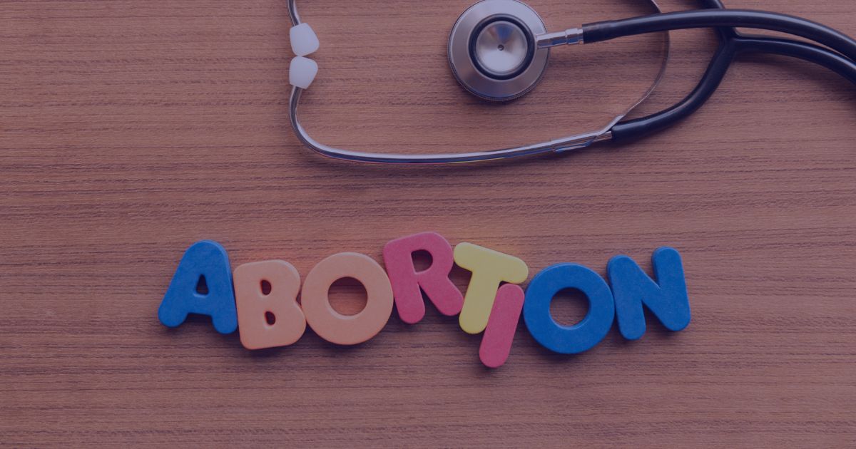 Colorful letters spelling "abortion" next to a stethoscope on a wooden table.