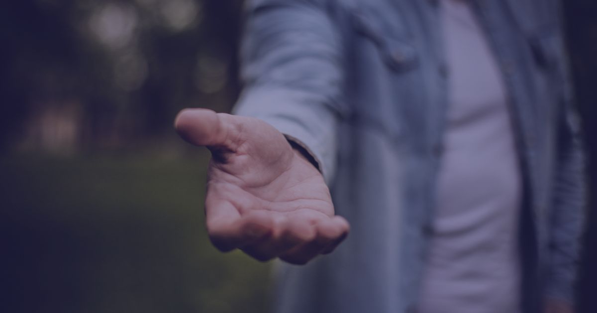 A hand reaches out towards the viewer with a blurred background.