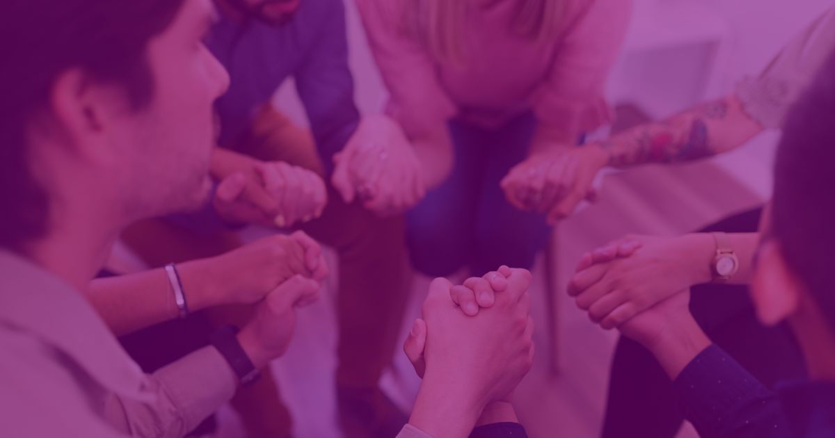 a group of people holding hands in a supportive manner, overlaid with a translucent purple filter