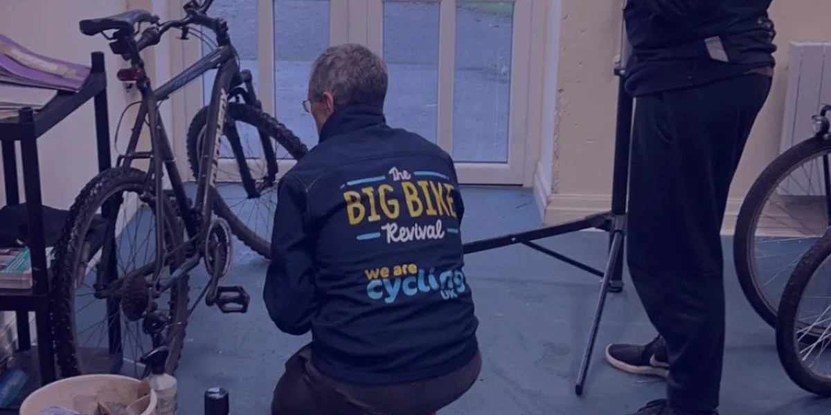 a man stood waiting whilst his bike is repaired by a bike mechanic