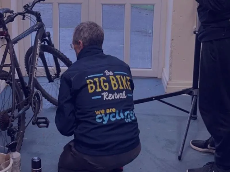 a man stood waiting whilst his bike is repaired by a bike mechanic