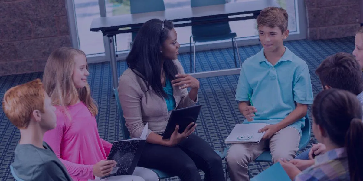 A group of children sitting in a circle with an adult facilitator, participating in a group activity