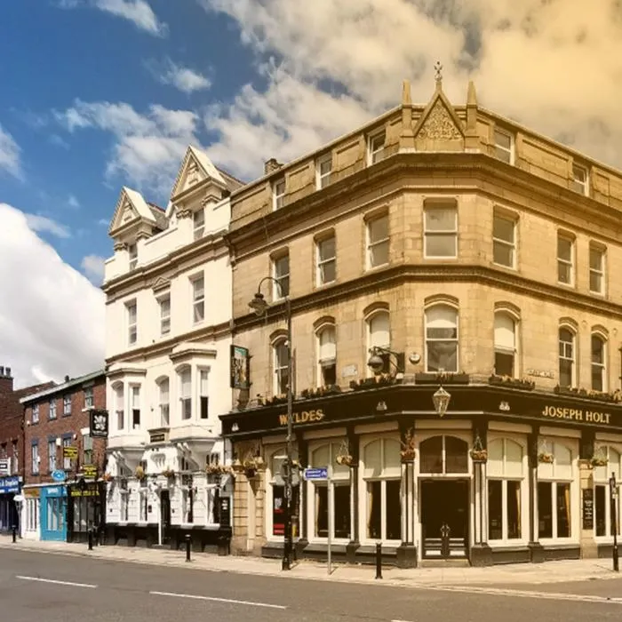 Street view of a traditional corner pub and neighbouring shops in a historic town centre, under a bright blue sky with scattered clouds