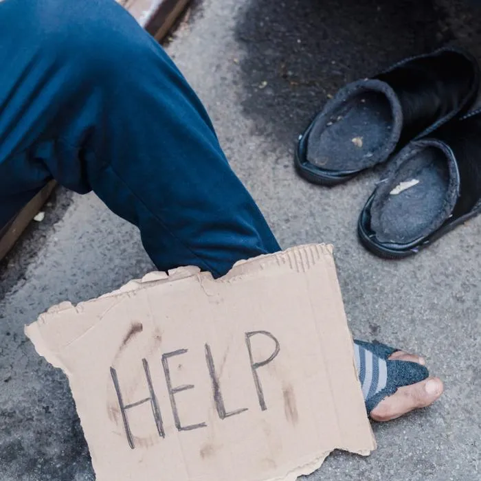 a handwritten sign with the word 'help' propped up by a mans leg wearing ripped clothing