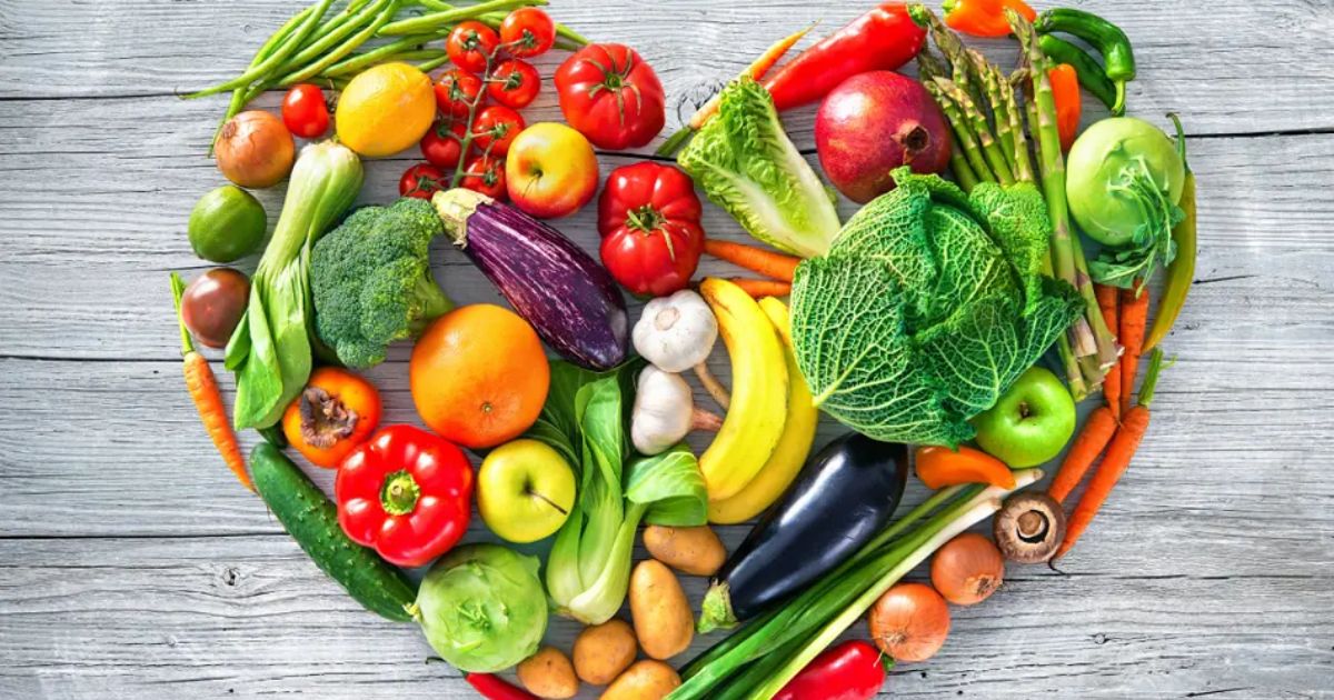 a variety of vibrant healthy fruit and veg laid out in a heart shape on a wooden backdrop