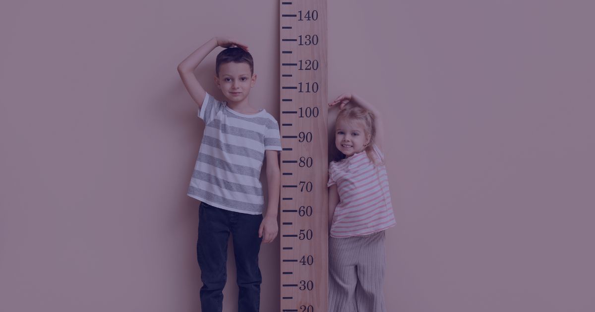 two young children stood either side of a large ruler measuring their growth