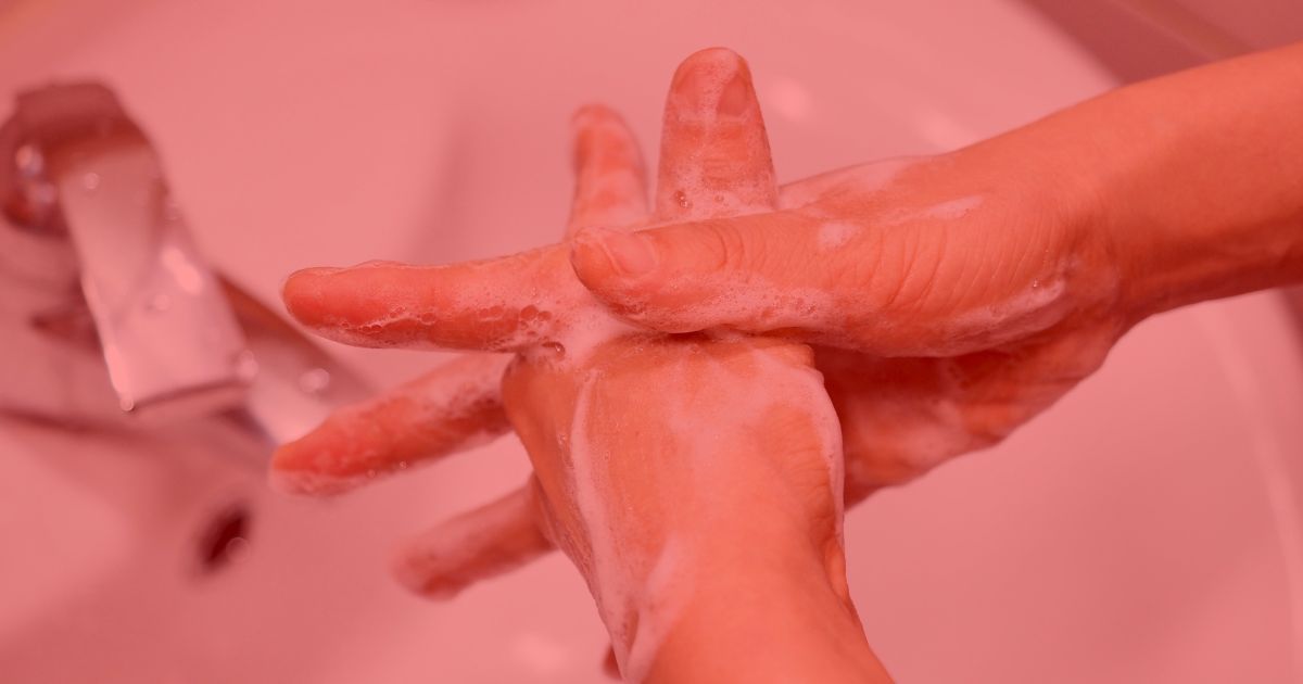 a person washing their hands with plenty of soap and water, the image is over laid with a transparent red filter.
