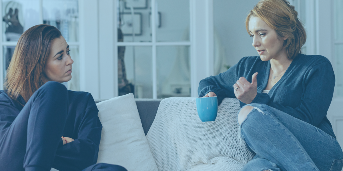 Two people sitting on a sofa having a conversation, with one person holding a blue mug