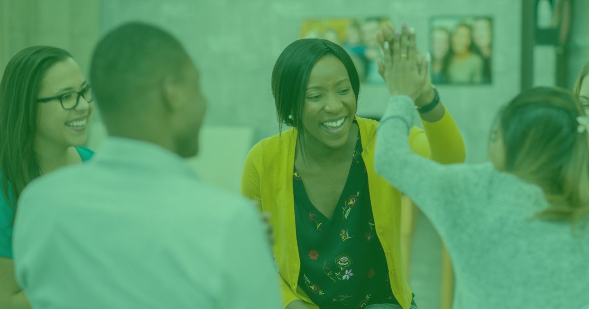 a group of adults sat together in a supportive environment, laughing, smiling and high fiving