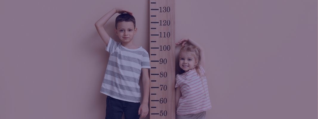 two young children stood either side of a large ruler measuring their growth
