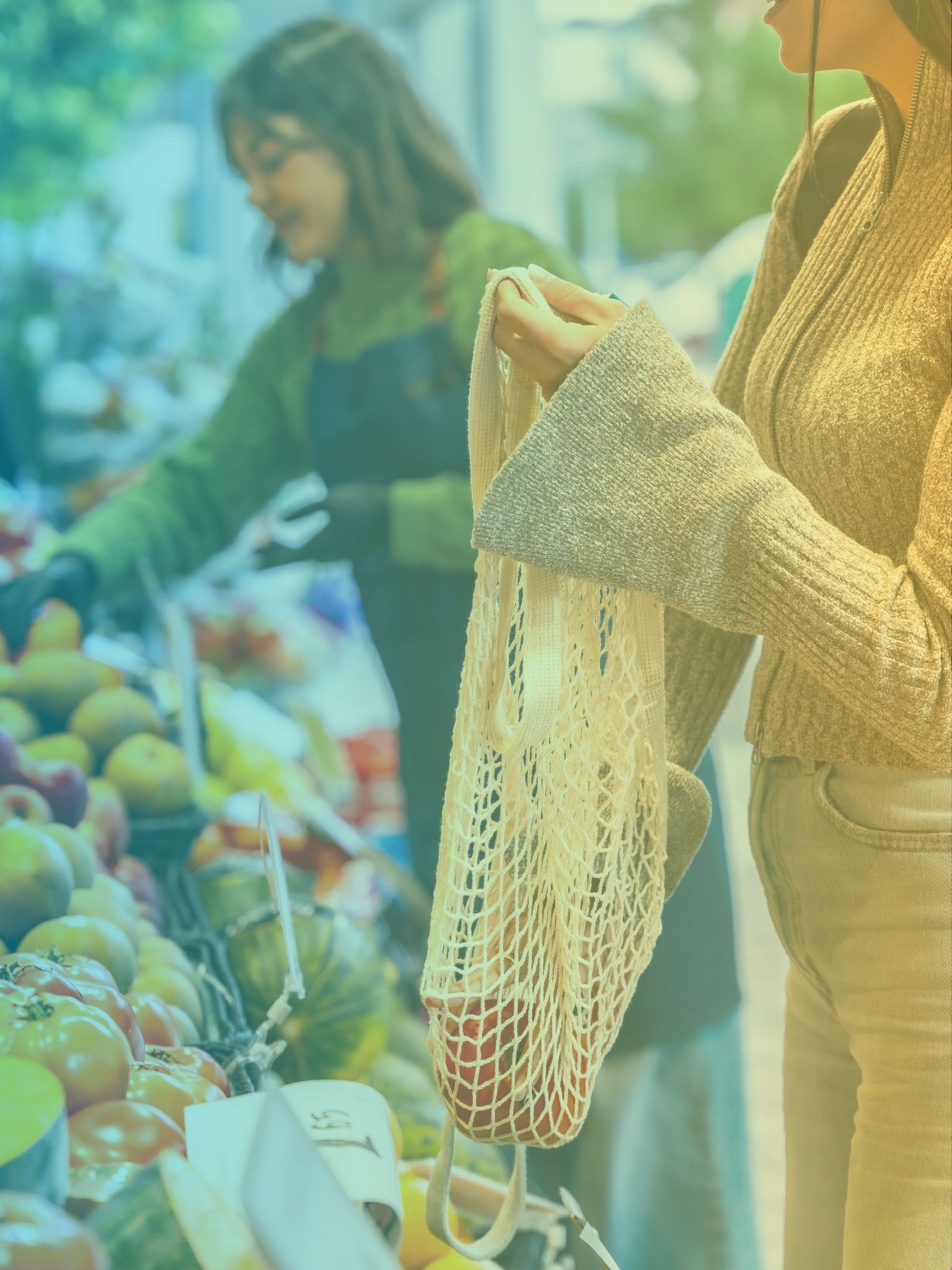 a woman with a cotton shopping bag picking organic produce from a market stall