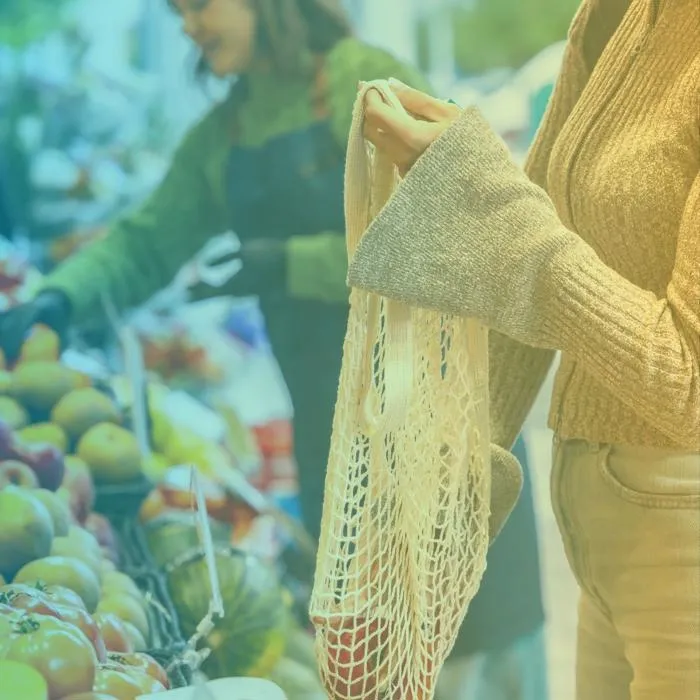 a woman with a cotton shopping bag picking organic produce from a market stall