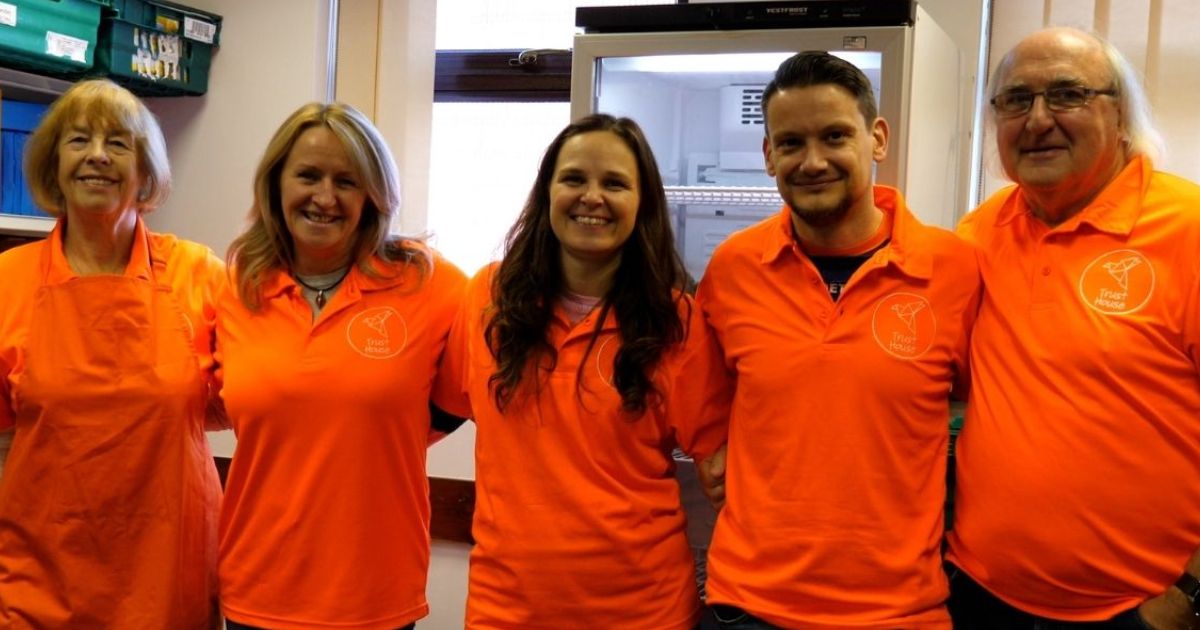 5 volunteers from Trust House Bury wearing their orange uniform and smiling for the camera