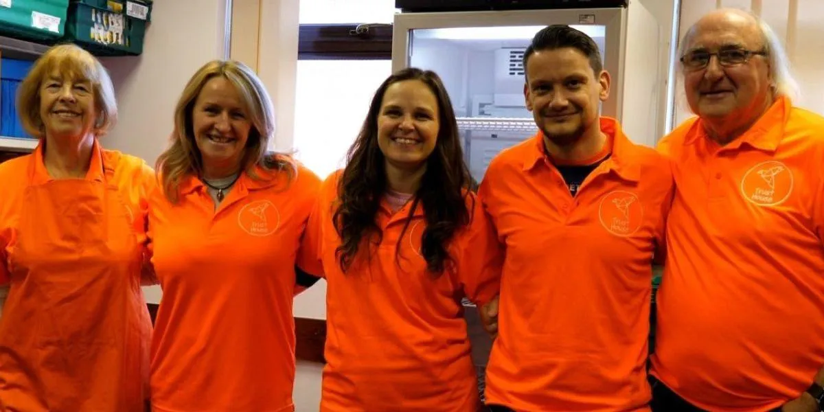 5 volunteers from Trust House Bury wearing their orange uniform and smiling for the camera