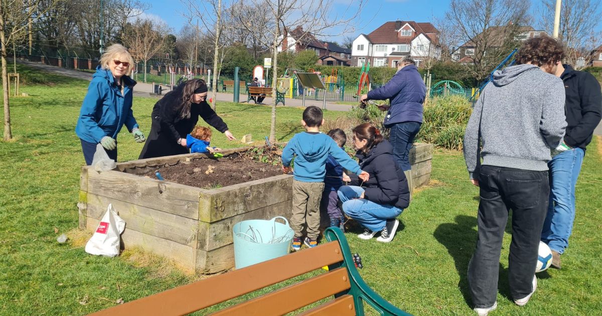 adults and children gather around a planter in a local park