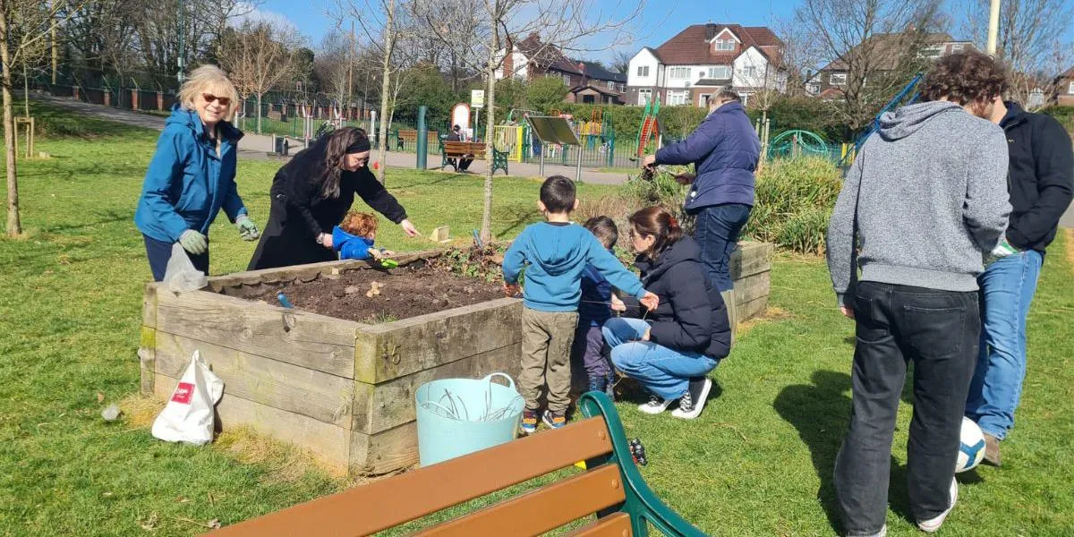 adults and children gather around a planter in a local park