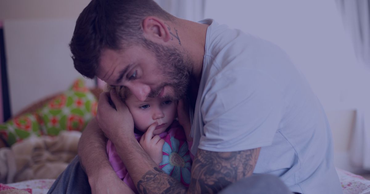 A tattooed adult gently hugging a young child in a cozy, home setting.