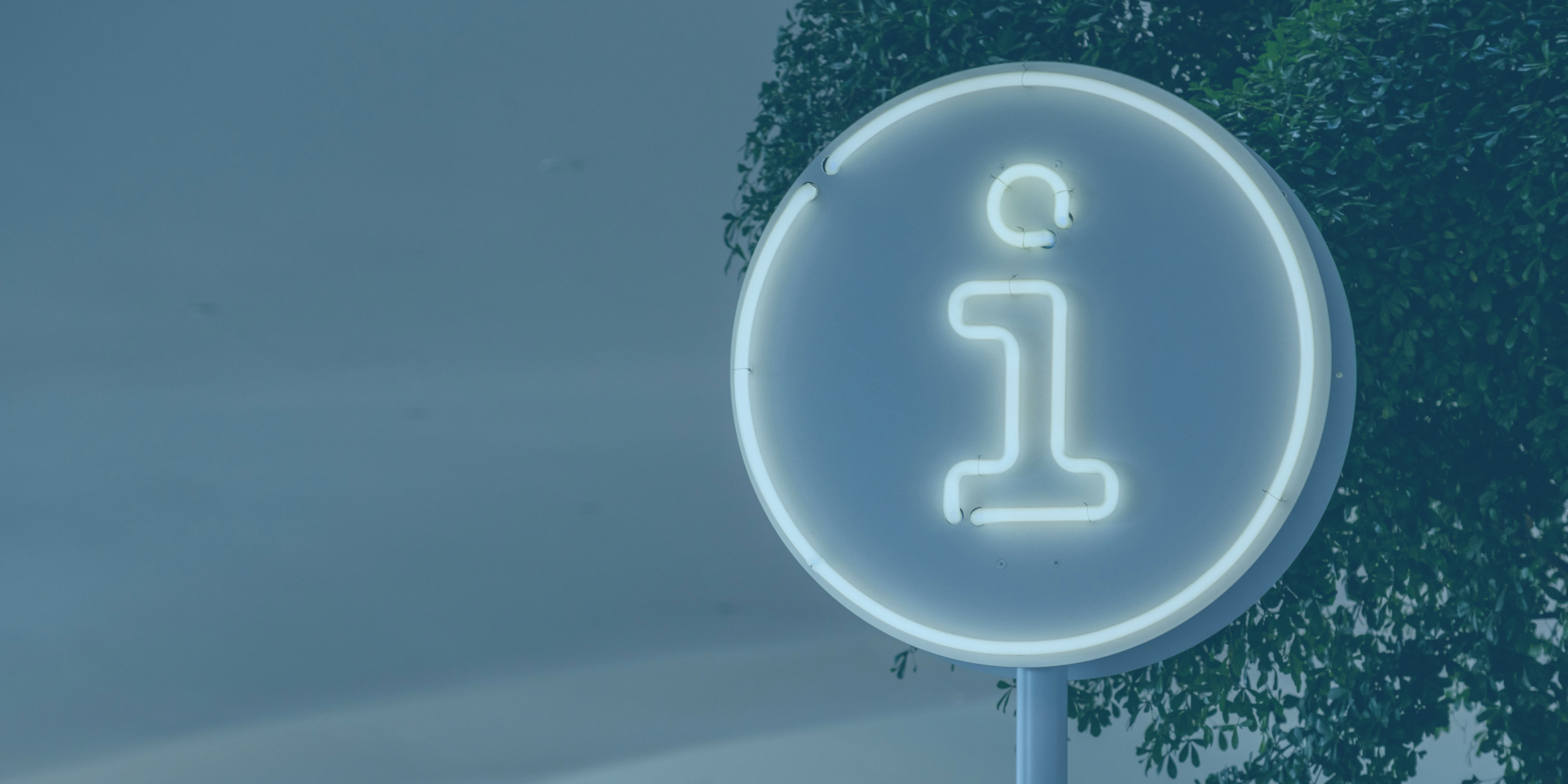 Illuminated information symbol sign in a circular frame, positioned near green foliage