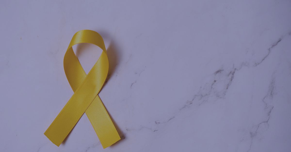 Yellow awareness ribbon on a marble background symbolizing suicide prevention and mental health awareness.