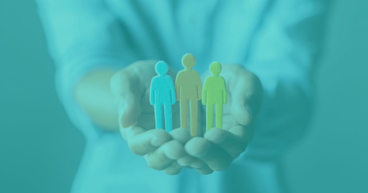 A person holding three colorful paper cut-out figures in their open hands, symbolizing support and community.