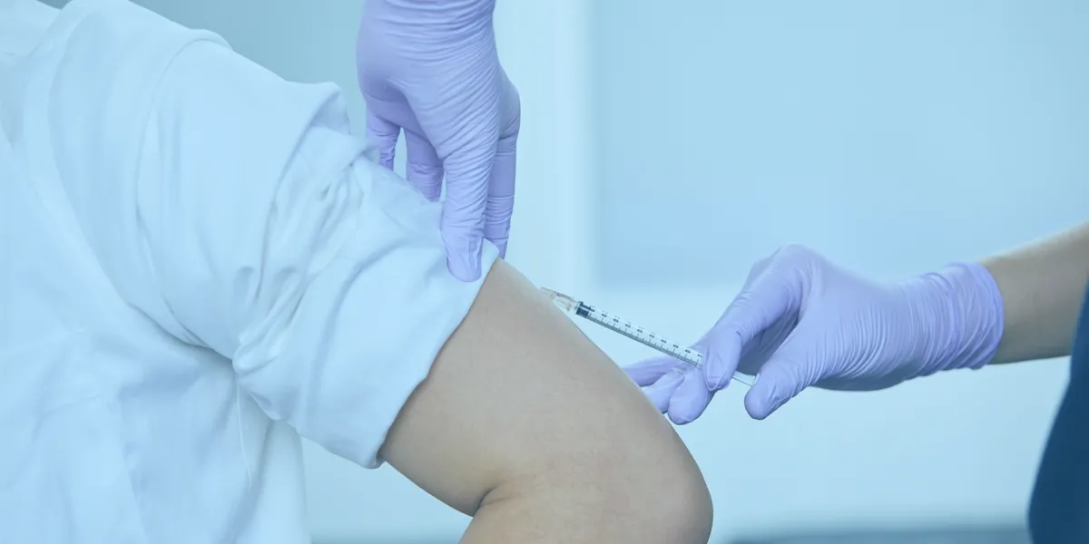 Close-up of a healthcare professional wearing purple gloves administering an injection into a person’s upper arm.