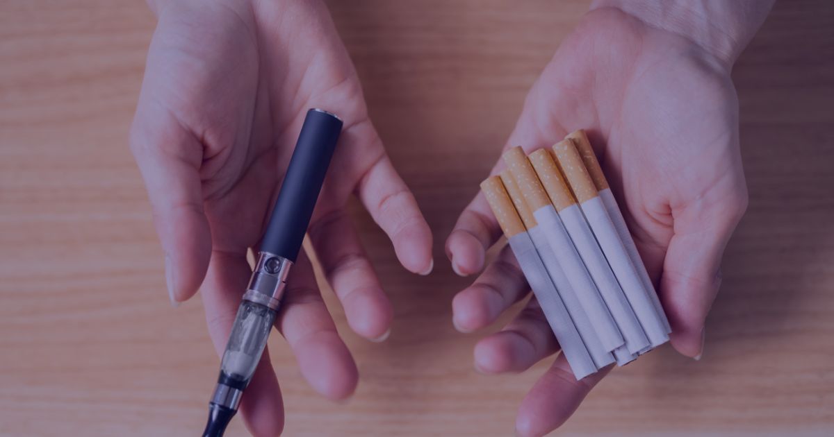 A person with open hands, holding a vape device in one hand and a number of unlit cigarettes in the other