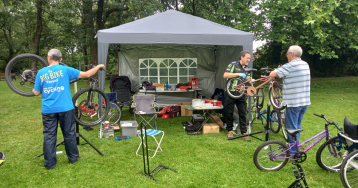 3 men gathering around and repairing numerous bicycles in a park
